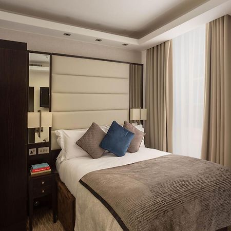 Montcalm Brewery Townhouse Hotell London Exteriör bild The image shows a cozy bedroom. It features a comfortable double bed with a light-colored duvet and decorative pillows in shades of blue and gray. The headboard is upholstered in a soft material, and there are bedside lamps on either side of the bed.