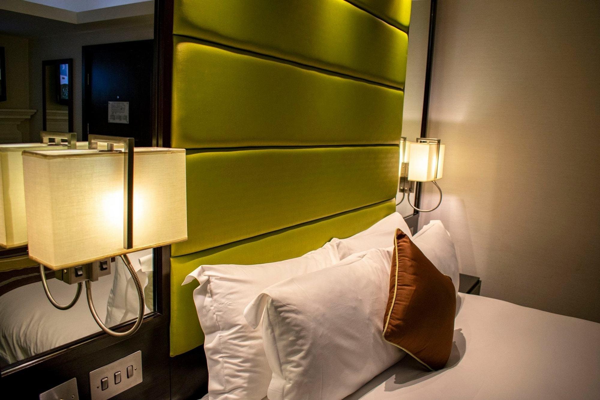 Montcalm Brewery Townhouse Hotell London Exteriör bild The photo shows a modern hotel room with a stylish design. The focal point is a large bed with white pillows and a decorative brown pillow. The headboard is bright green and has a textured appearance. On either side of the bed, there are wall lamps t