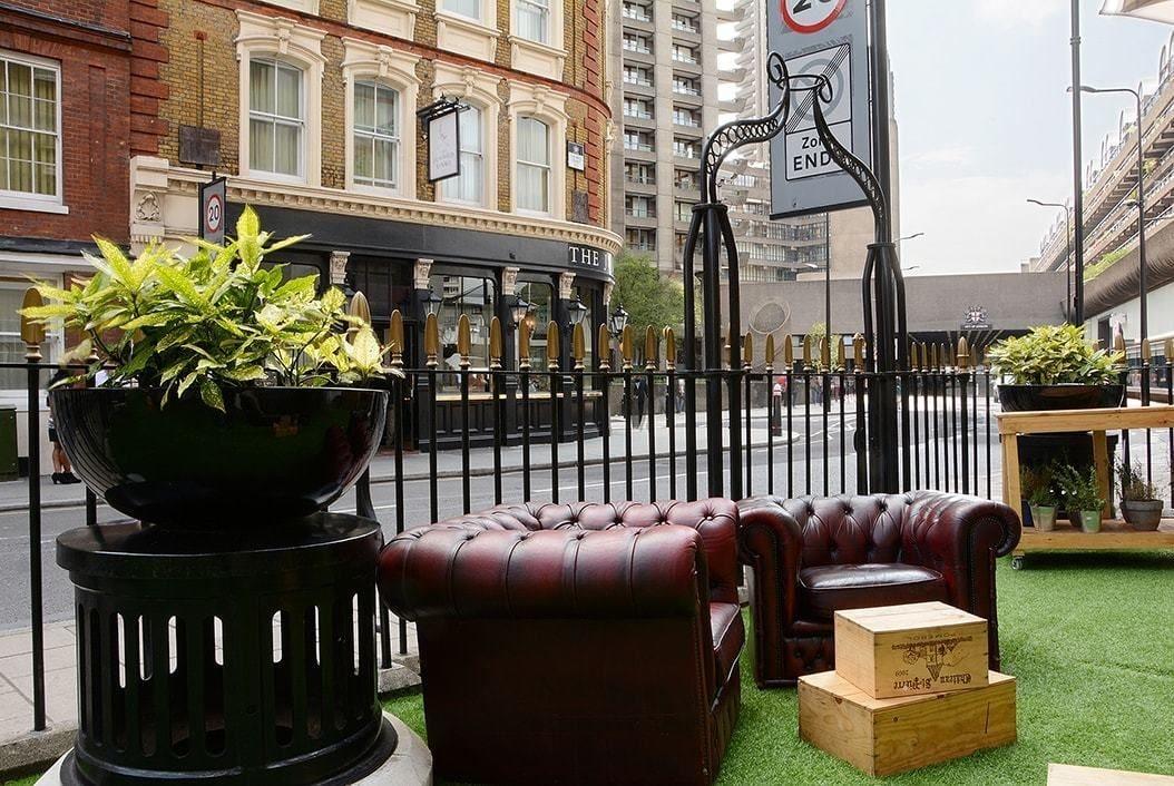 Montcalm Brewery Townhouse Hotell London Exteriör bild The photo shows a street scene with a cozy outdoor seating area. There are two plush, dark leather couches arranged on green grass, creating a welcoming atmosphere. Surrounding the seating are large planters with vibrant plants. In the background, th