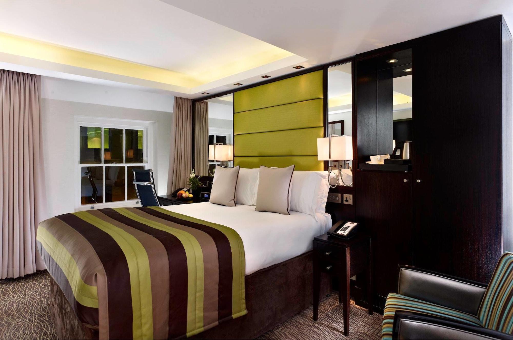 Montcalm Brewery Townhouse Hotell London Exteriör bild The photo shows a modern hotel room featuring a large bed with a striped comforter in shades of green, brown, and cream. The bed is adorned with several decorative pillows. Behind the bed, there is a contemporary headboard with a green panel design. 