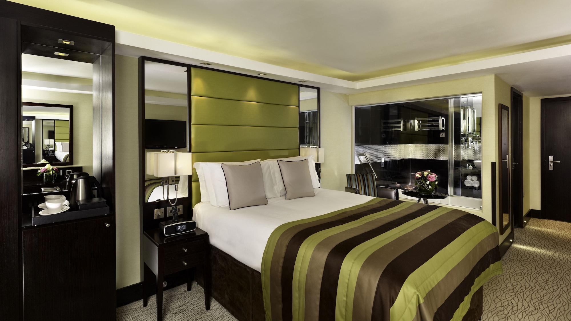 Montcalm Brewery Townhouse Hotell London Exteriör bild The photo shows a modern hotel room designed with a sophisticated aesthetic. It features a comfortable double bed with a striped brown and green bedspread, complemented by two light gray decorative pillows. Behind the bed is an elegant headboard sect