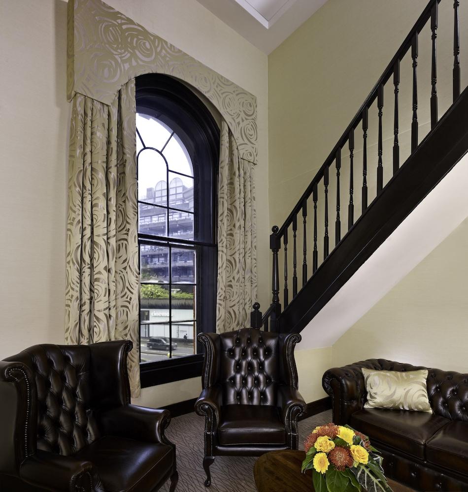 Montcalm Brewery Townhouse Hotell London Exteriör bild The photo shows a cozy interior space featuring two elegant leather armchairs placed near a large, ornate window with arched top and decorative curtains. The wall is painted in a muted color, enhancing the warmth of the room. A staircase with black s