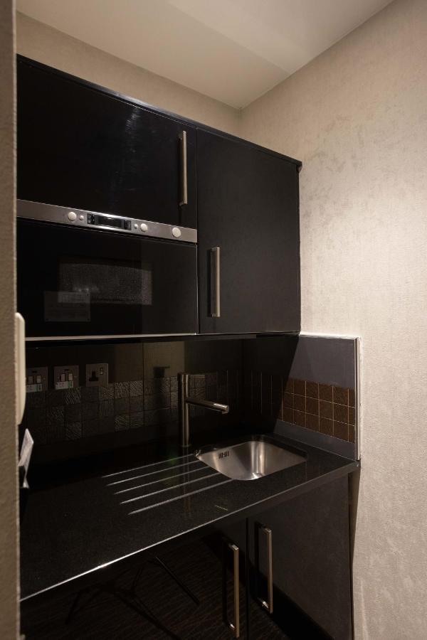 Montcalm Brewery Townhouse Hotell London Exteriör bild The photo shows a modern kitchen setup with a dark color scheme. It features:

- A built-in microwave oven situated above a countertop.
- A sleek black cabinet beneath the microwave, which likely stores kitchen items.
- A stainless steel sink placed 