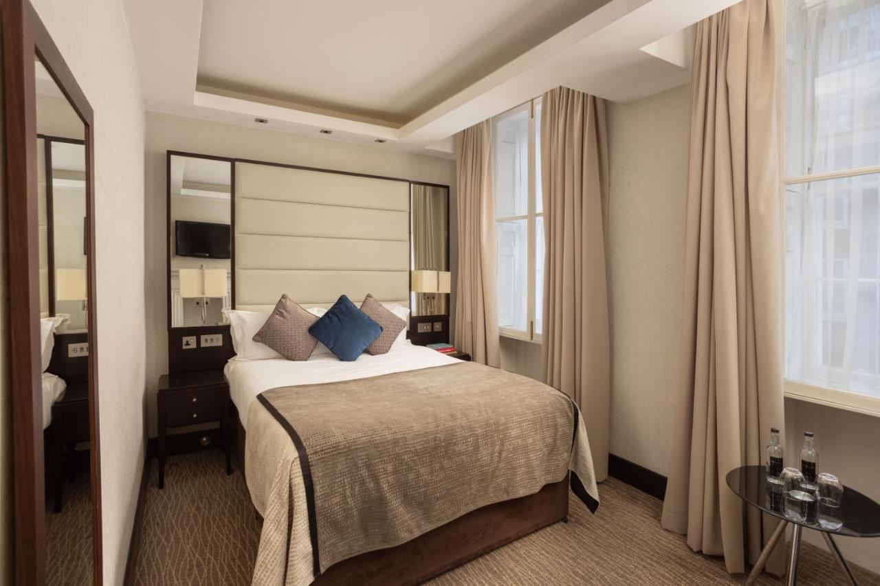 Montcalm Brewery Townhouse Hotell London Exteriör bild The photo shows a cozy hotel bedroom. The room features a neatly made double bed with a beige bedspread and decorative pillows, including a blue one. There are bedside tables on either side of the bed with lamps. The walls are painted in a soft color