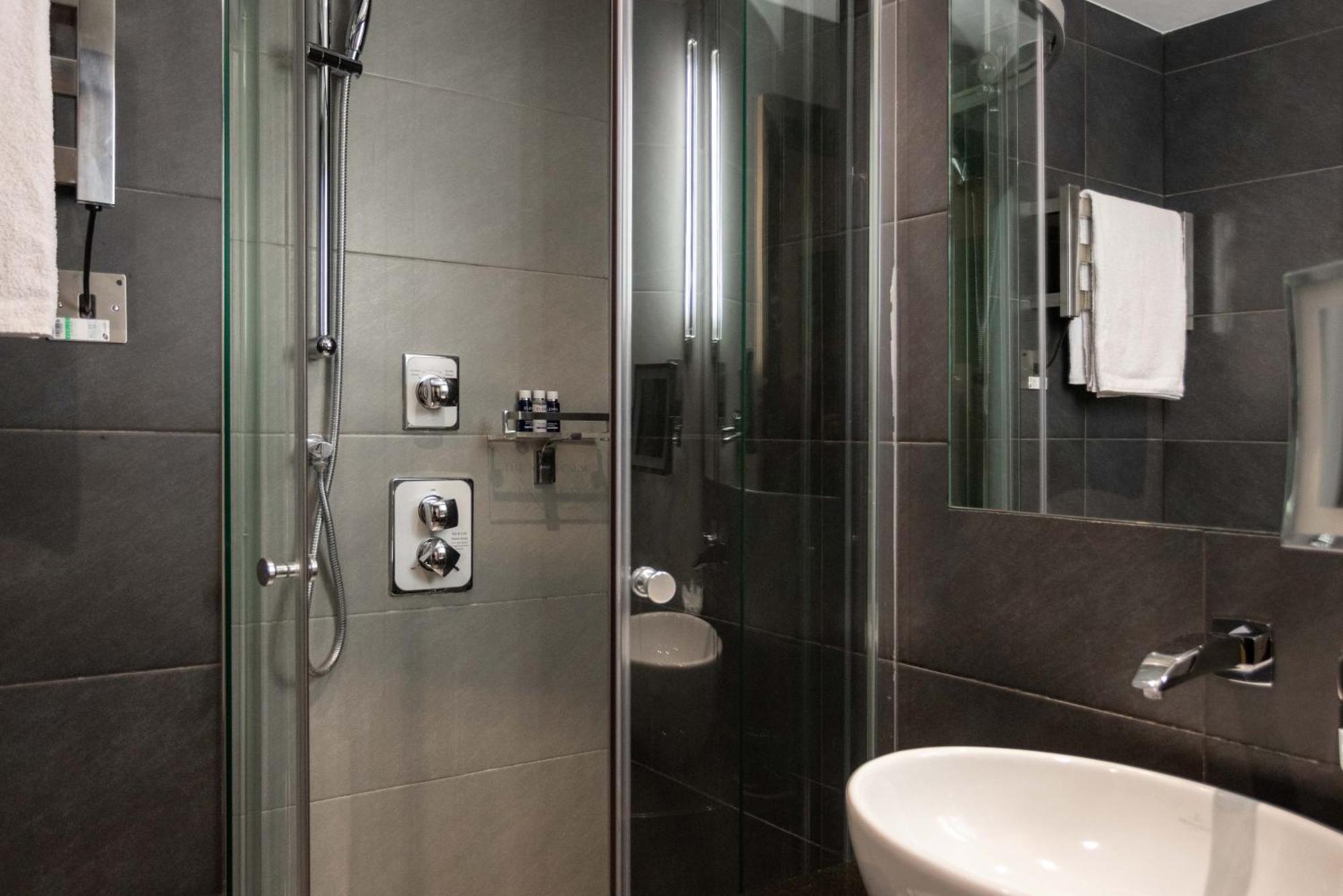 Montcalm Brewery Townhouse Hotell London Exteriör bild The photo shows a modern bathroom with a glass shower enclosure. The shower features a handheld showerhead and various controls mounted on the wall. The walls are tiled in dark, sleek tones, contributing to a contemporary aesthetic. There is a round 