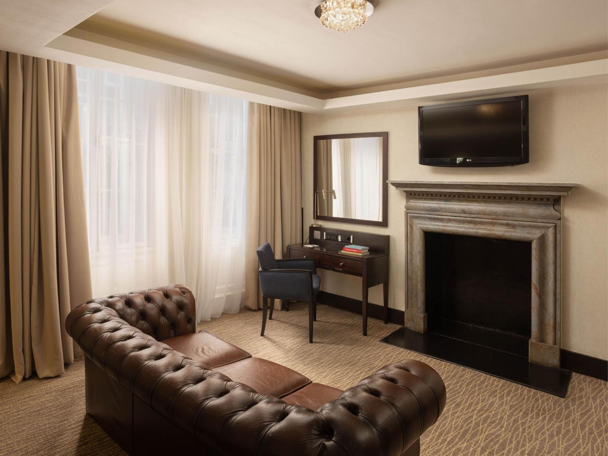 Montcalm Brewery Townhouse Hotell London Exteriör bild The photo shows a cozy and elegantly designed room. There is a comfortable brown leather sofa with tufted detailing. A small desk and chair are positioned near a mirror, providing a space for work or personal grooming. On the wall, a flat-screen TV i