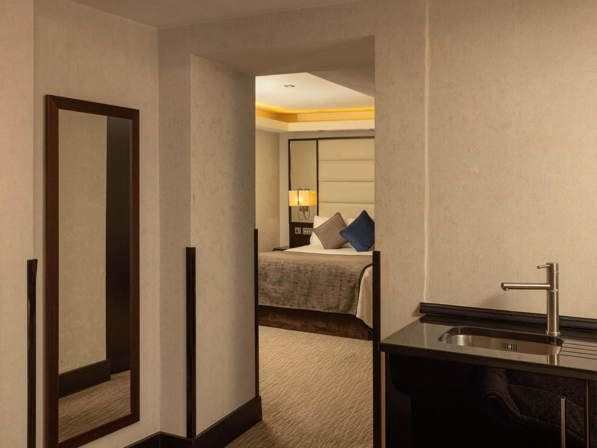 Montcalm Brewery Townhouse Hotell London Exteriör bild The photo shows an interior space that appears to be a hotel room or a suite. There is a doorway leading to a bedroom visible in the background, where a bed with decorative pillows can be seen. To the side, there is a small wet bar or kitchenette are