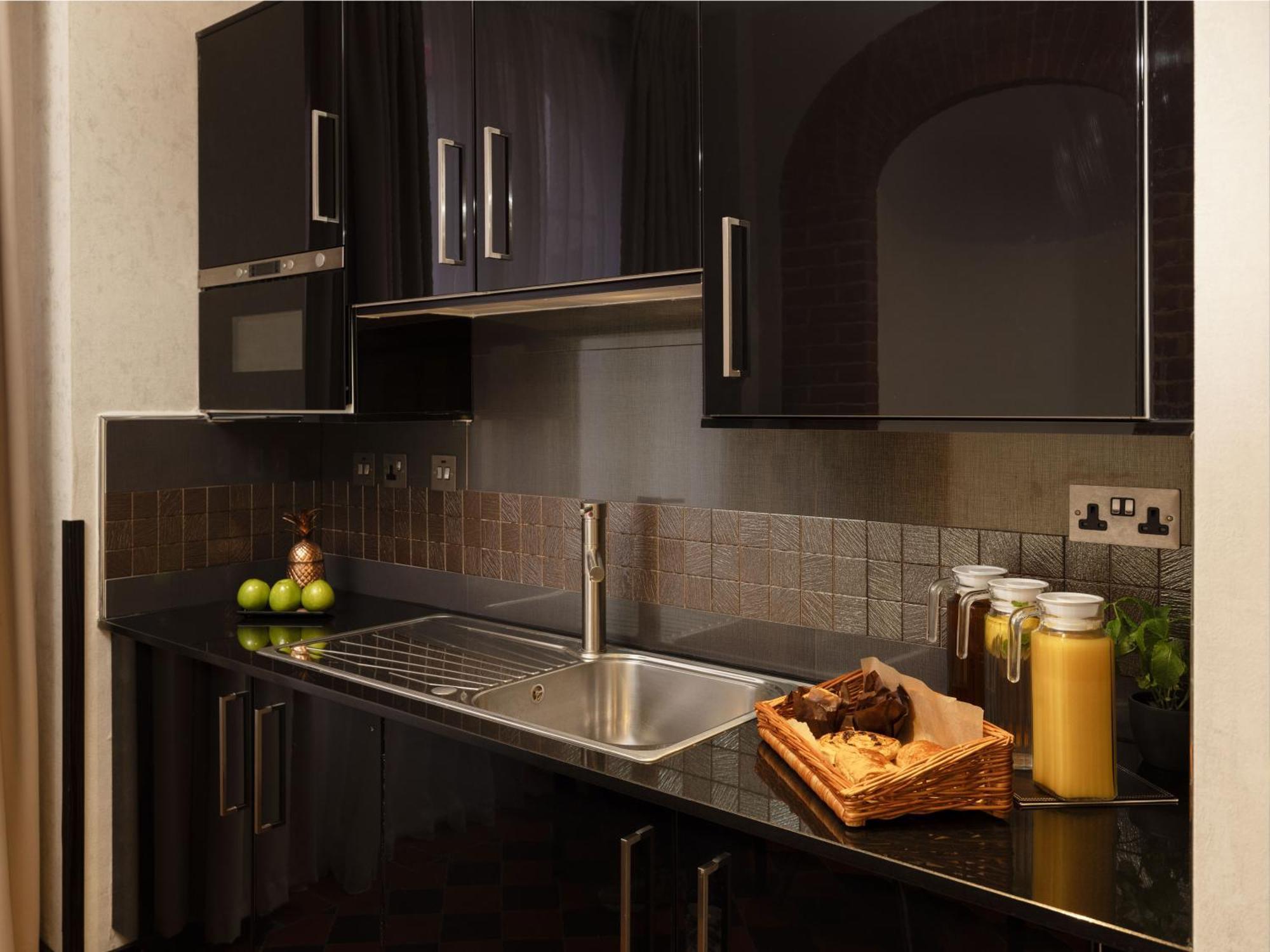 Montcalm Brewery Townhouse Hotell London Exteriör bild The photo shows a modern kitchen with sleek black cabinetry and a glossy finish. The kitchen features a stainless steel sink with a contemporary faucet, set against a dark, textured countertop. Above the counter, there are cabinets that match the cou