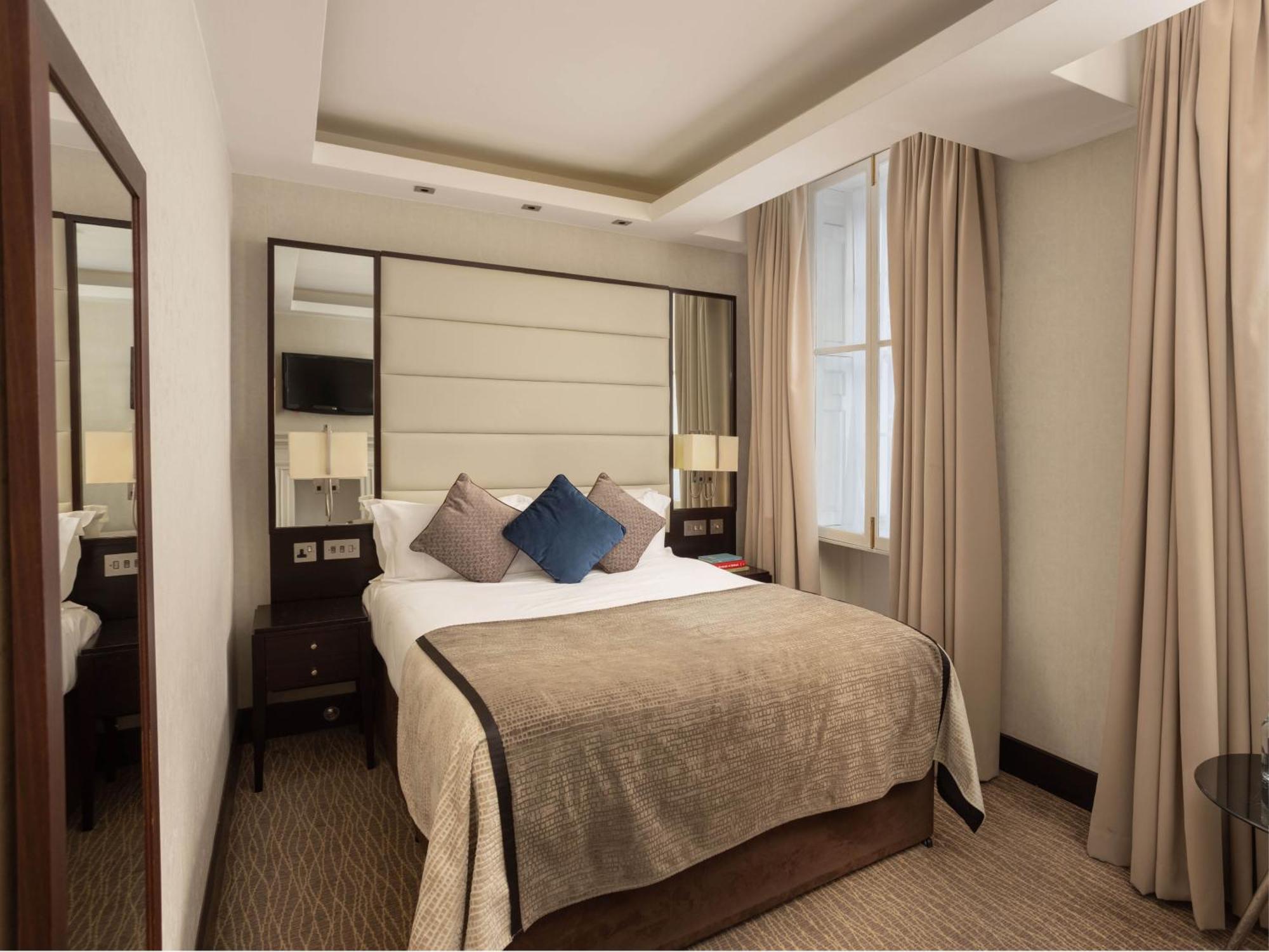 Montcalm Brewery Townhouse Hotell London Exteriör bild The photo shows a cozy hotel room with a bed as the focal point. The bed is made with neutral-colored linens and has several pillows, including a decorative blue one. There are bedside tables on either side of the bed, each with a lamp. A large mirro