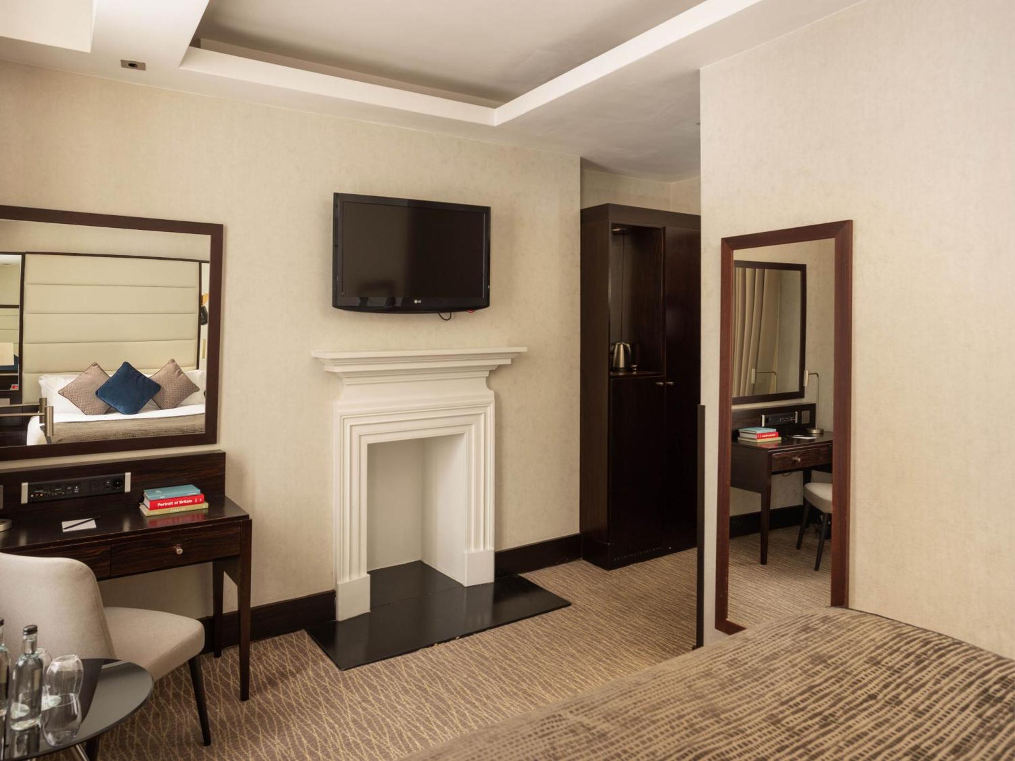 Montcalm Brewery Townhouse Hotell London Exteriör bild The photo depicts a stylish hotel room. It features a double bed, a large flat-screen TV mounted on the wall, and a decorative fireplace. There is a wooden desk with a chair beside it, as well as a mirror hanging on the wall. The decor is modern and 