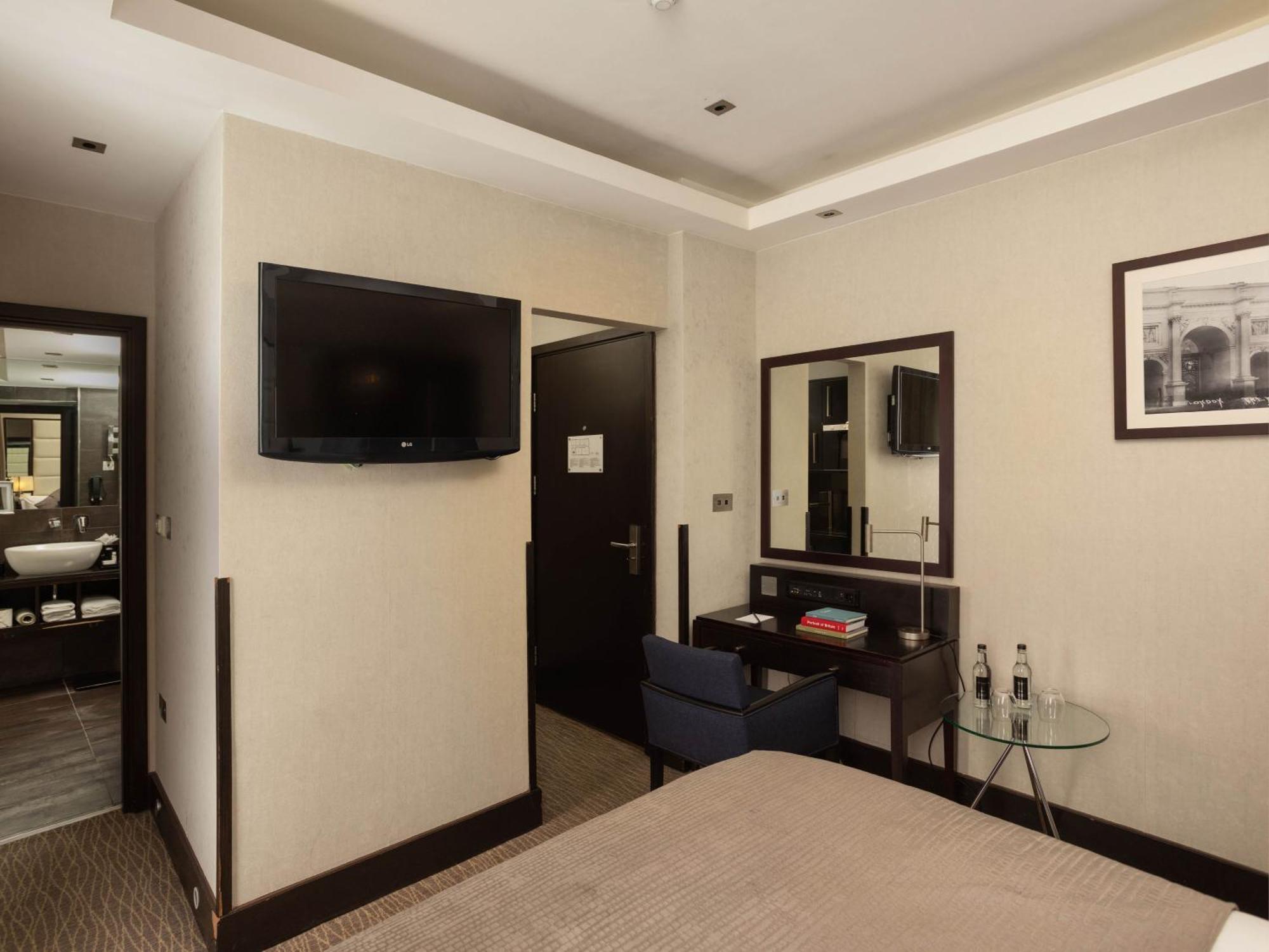 Montcalm Brewery Townhouse Hotell London Exteriör bild The photo shows a hotel room with a modern and minimalist design. On the left, there's a wall-mounted flat-screen TV. In the center, there's a bed with a neutral-colored bedspread. To the right of the bed, there is a small desk with a mirror above it