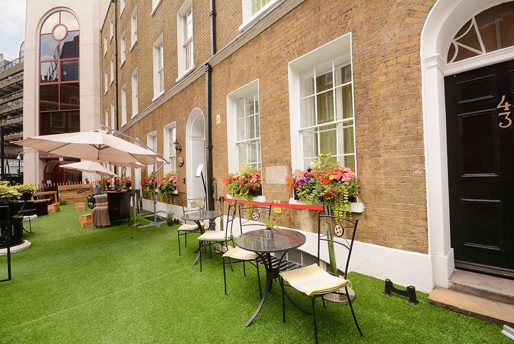 Montcalm Brewery Townhouse Hotell London Exteriör bild The photo depicts a charming outdoor area in front of a building with a warm, textured brick facade. There is a neatly maintained lawn, likely made of artificial grass, and several small round tables with chairs are arranged outside. Flower pots with