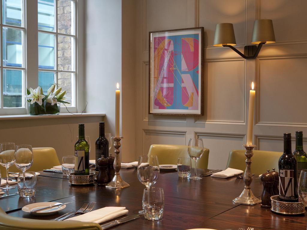 Montcalm Brewery Townhouse Hotell London Exteriör bild The photo shows an elegantly set dining room with a large wooden table surrounded by several chairs. The table is adorned with neatly arranged utensils, glasses, and decorative items. There are two tall candlesticks with candles and several bottles o