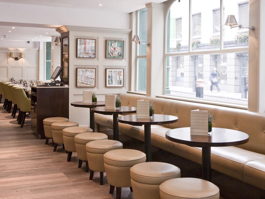 Montcalm Brewery Townhouse Hotell London Exteriör bild The photo displays a modern café or restaurant interior. There is a cozy seating area featuring light-colored, upholstered benches along the wall, accompanied by small round tables. The tables are paired with circular stools. The decor includes frame