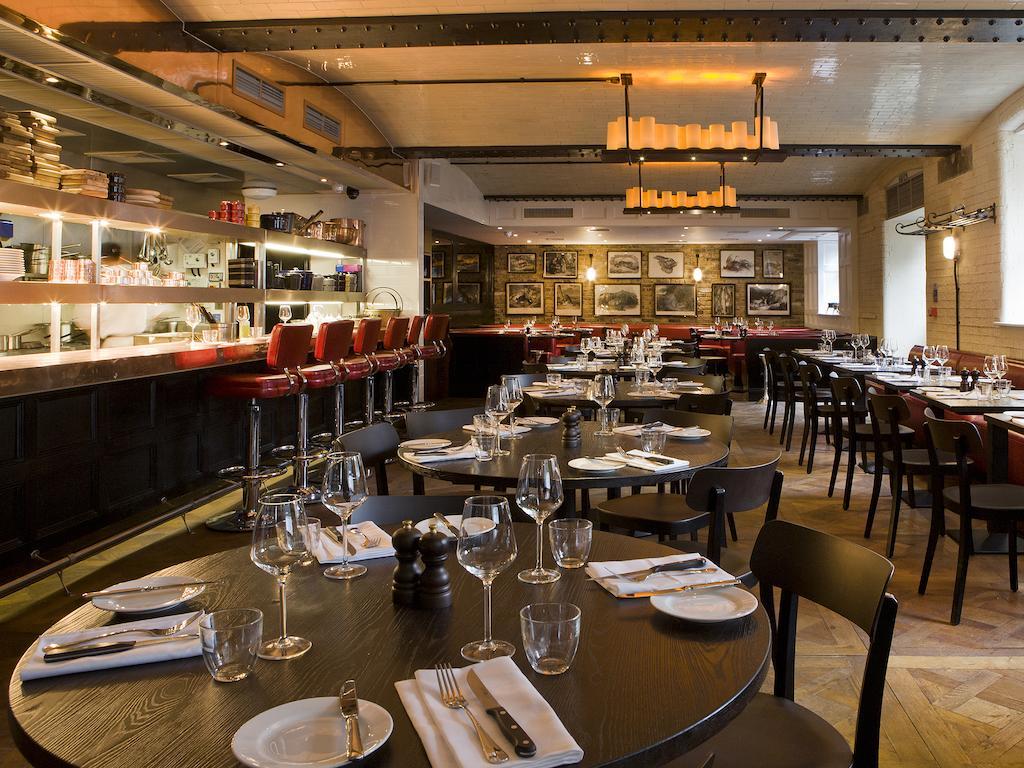 Montcalm Brewery Townhouse Hotell London Exteriör bild The photo shows the interior of a stylish restaurant. It features several round tables set with white plates, glasses, and silverware, all neatly arranged for dining. The decor includes a modern design with wooden floors and a mix of lighting fixture