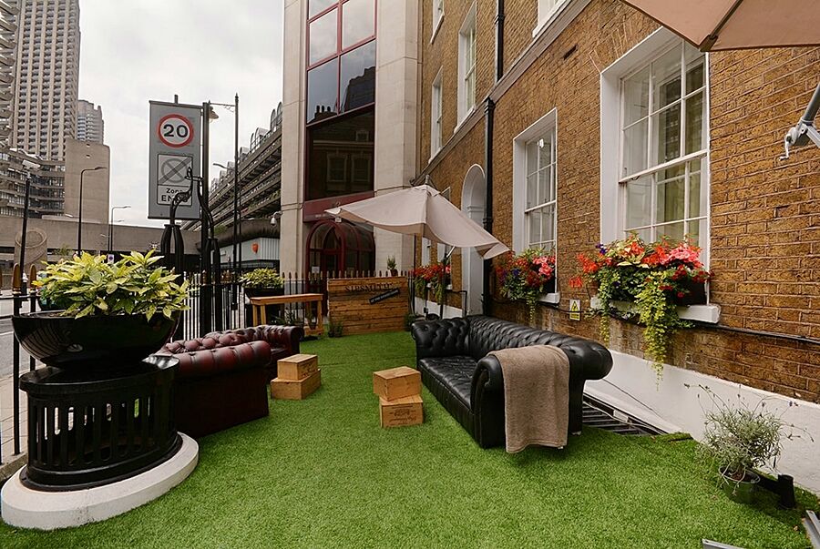 Montcalm Brewery Townhouse Hotell London Exteriör bild The photo depicts a charming outdoor space, likely a patio or garden area. It features two comfortable-looking leather sofas, one of which is a deep burgundy color, placed on a green artificial lawn. There are wooden crates that could serve as side t